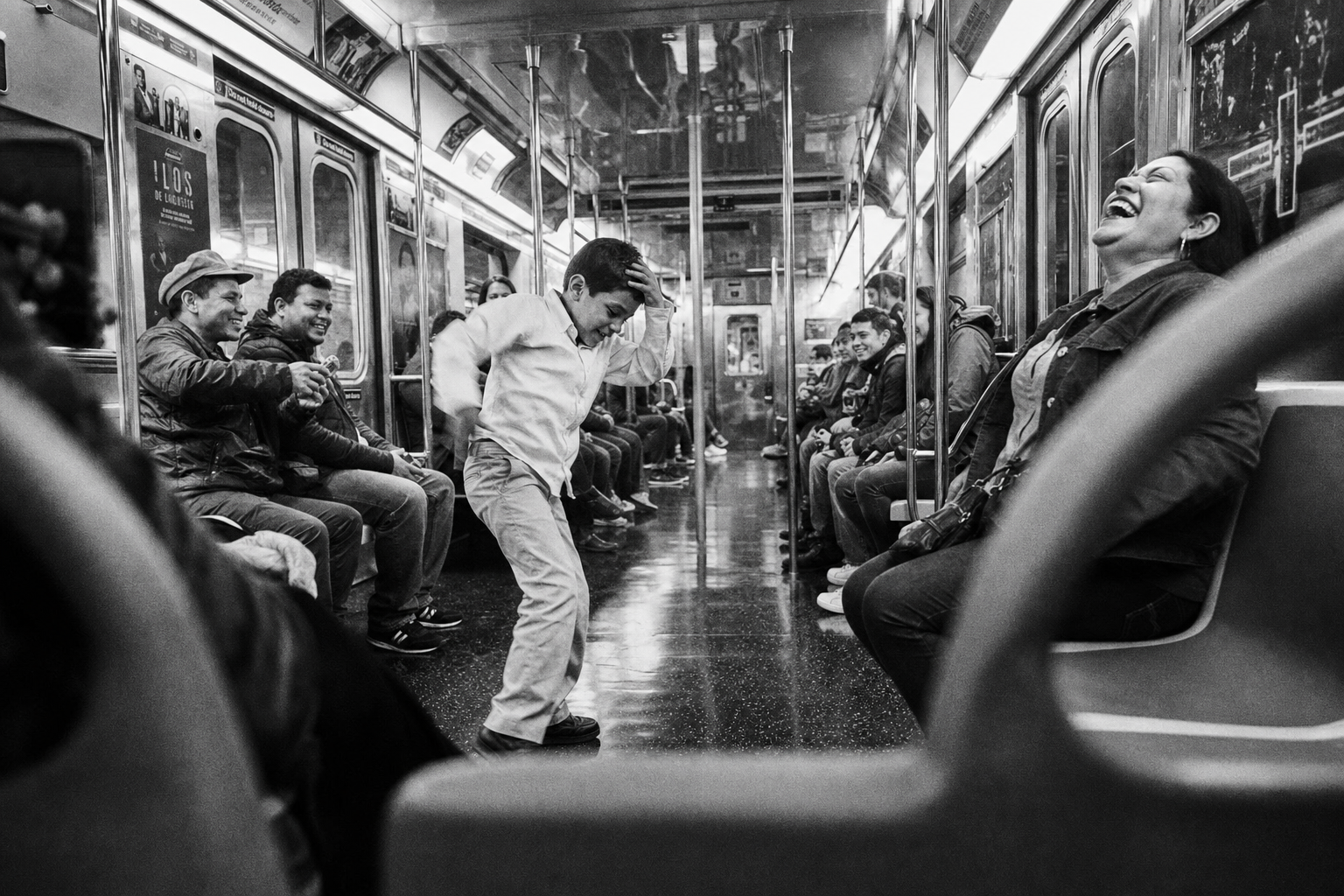 Jongen danst in het gangpad van een metrostel terwijl medereizigers lachend toekijken